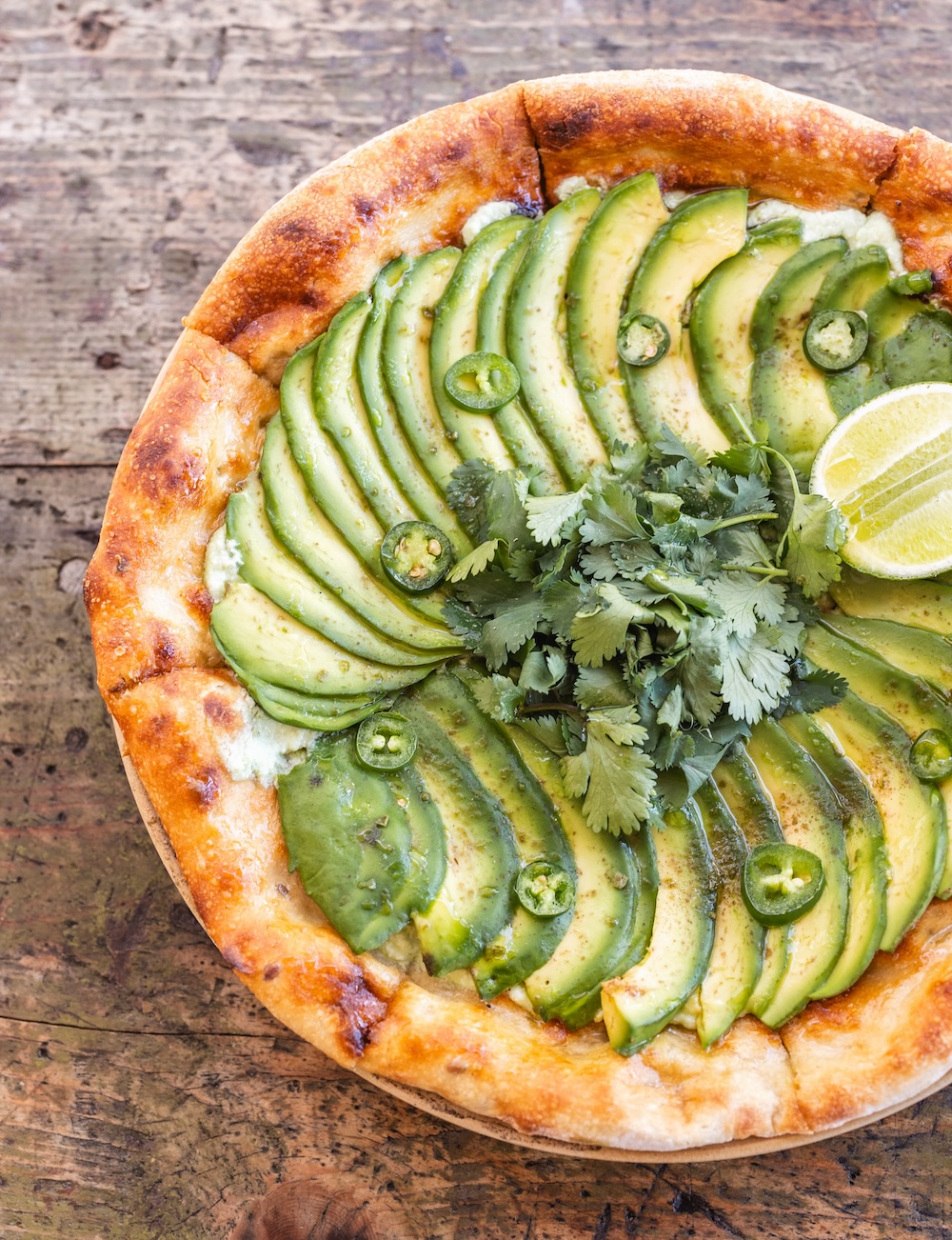 A wood fired pizza topped with Avocado, cilantro, lime, and jalapeno.